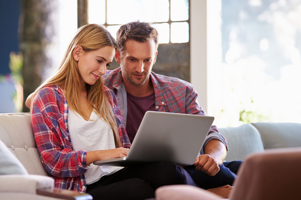 Preconception Couple At Home In Lounge Using Laptop Computer