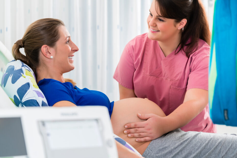 Happy pregnant woman in consultation room being examined by midwife