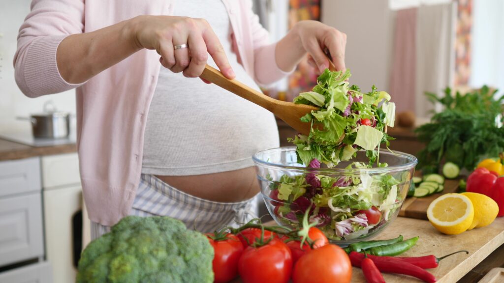 Pregnant woman preparing a meal in the kitchen making a salad for a healthy diet and nutrition