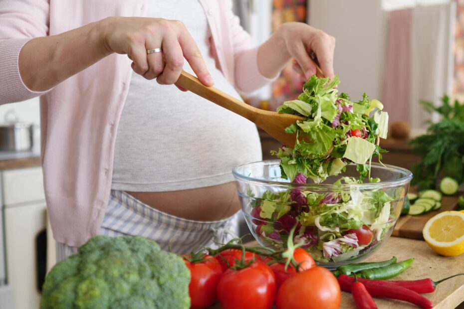 Pregnant woman preparing a meal in the kitchen making a salad for a healthy diet and nutrition