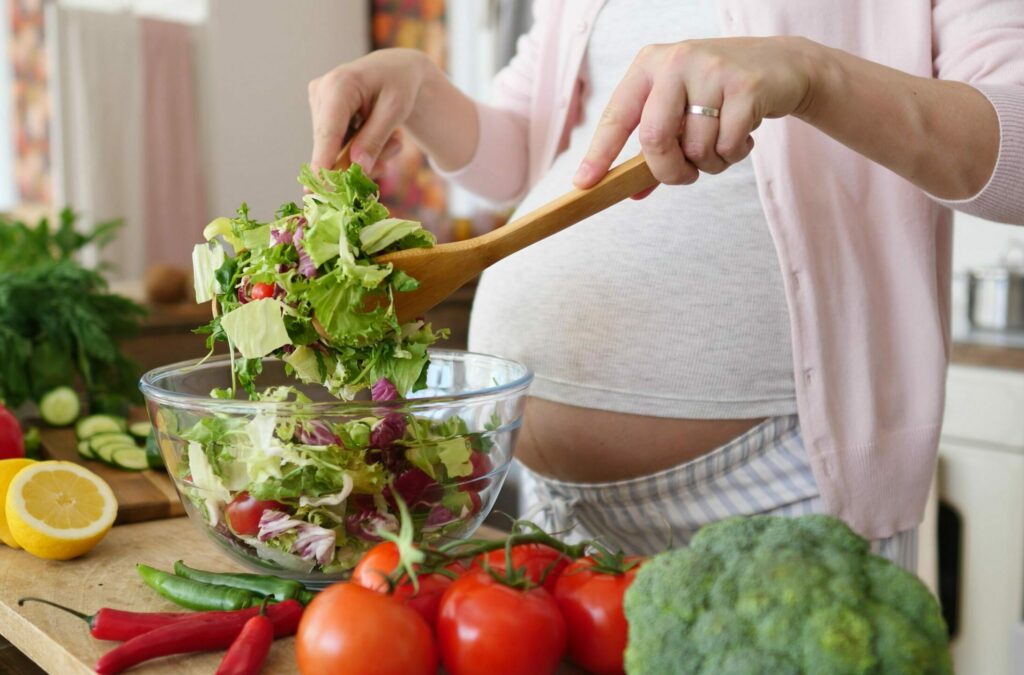 Pregnant woman preparing a meal in the kitchen making a salad for a healthy diet and nutrition