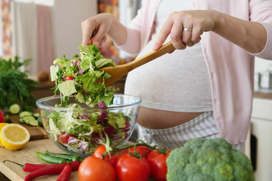 Pregnant woman preparing a meal in the kitchen making a salad for a healthy diet and nutrition