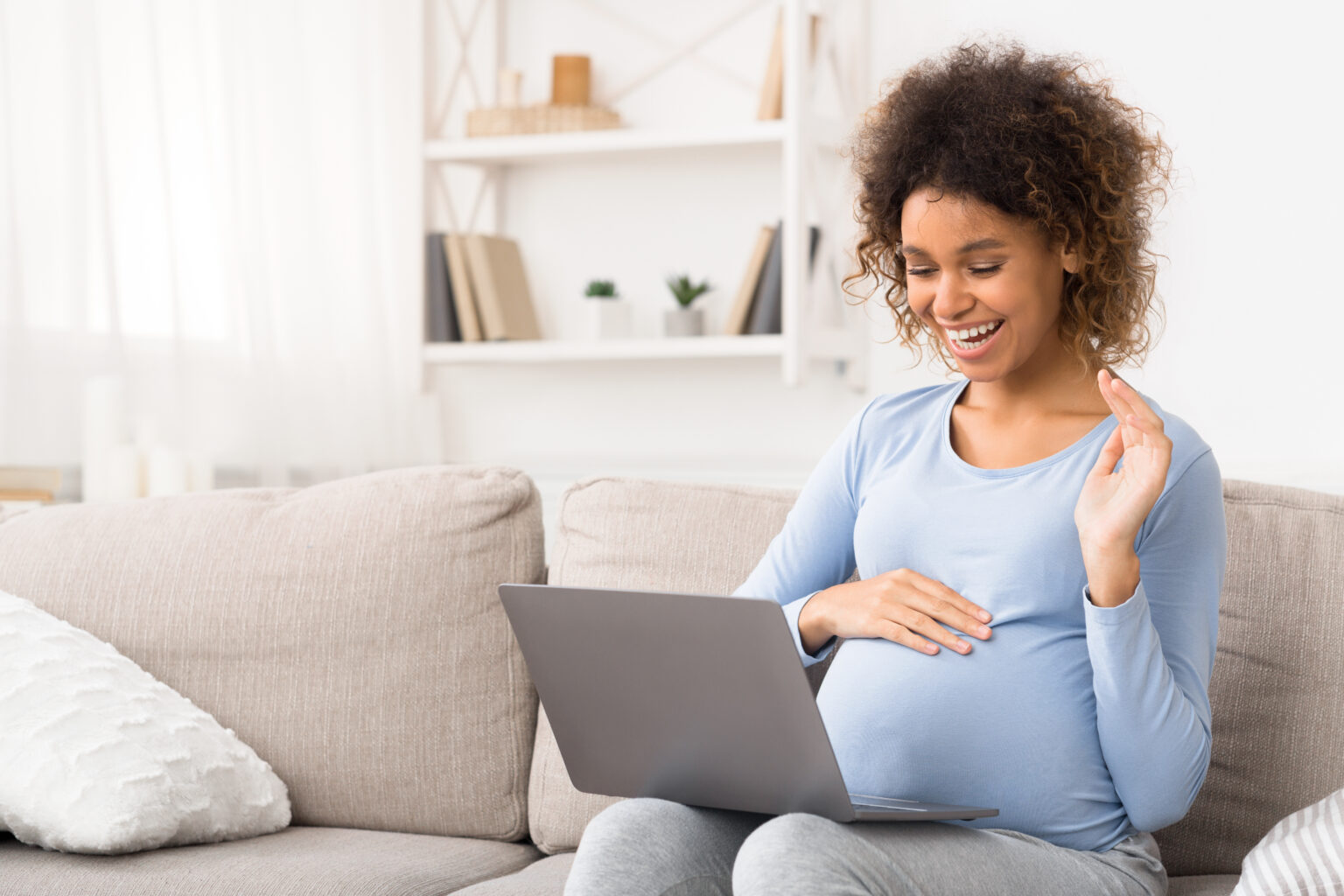 African American pregnant woman video chatting on laptop