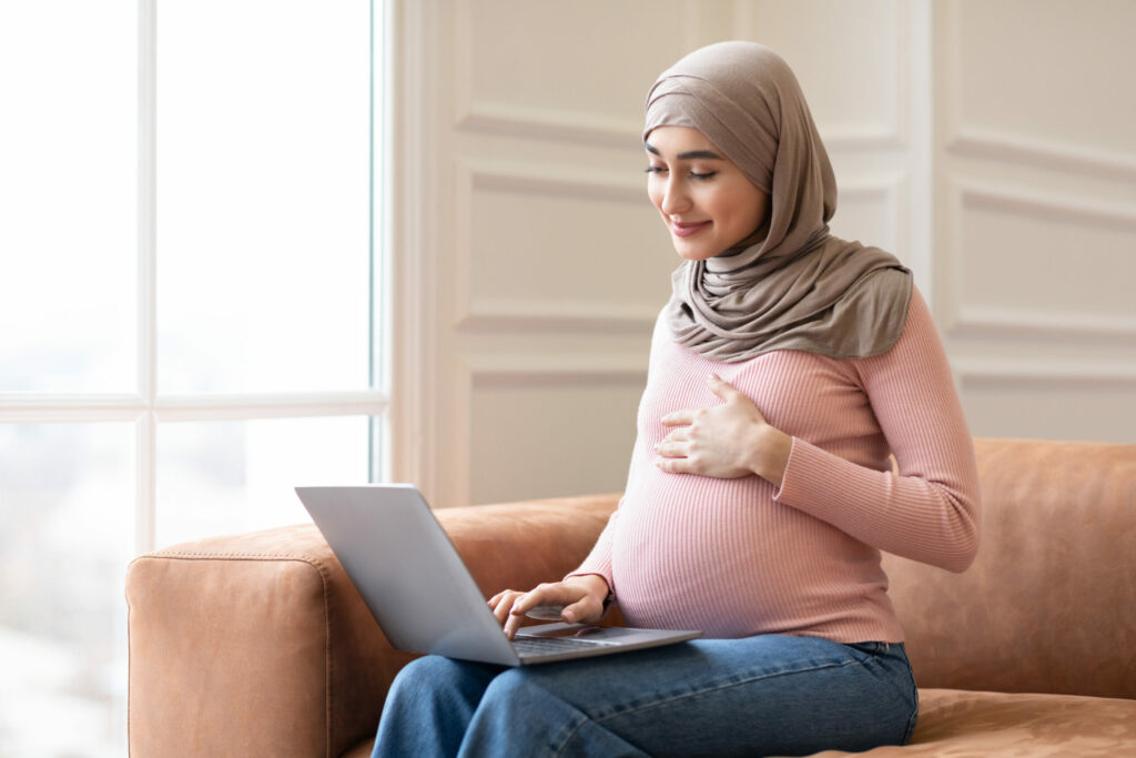 Pregnant woman using laptop sitting on couch at home