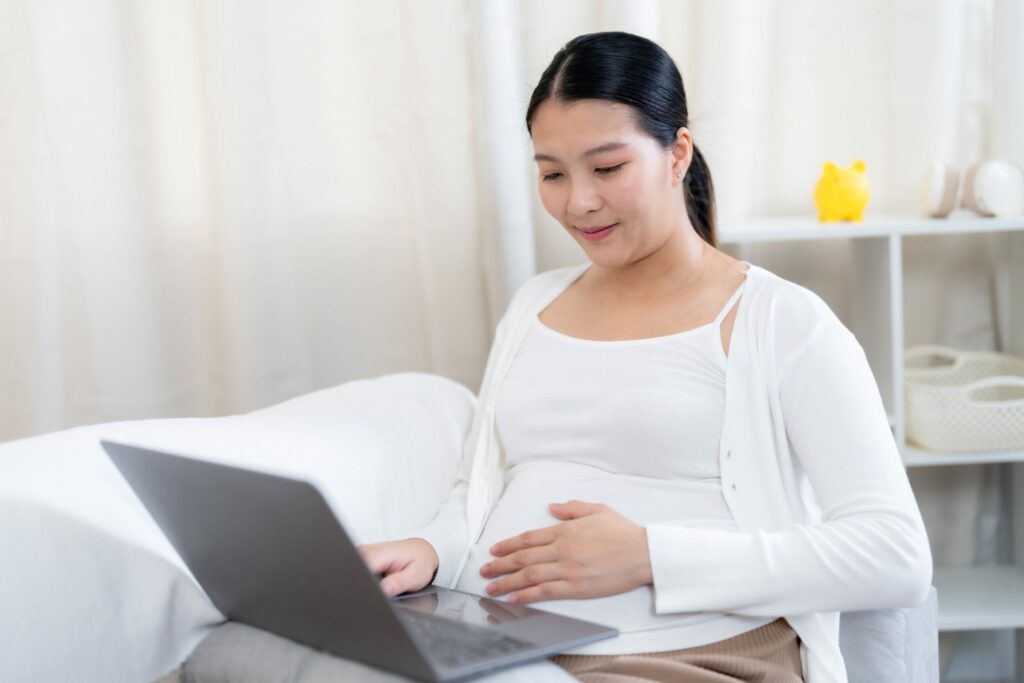 Healthy pregnant woman sat on a sofa using laptop with her hand on her bump