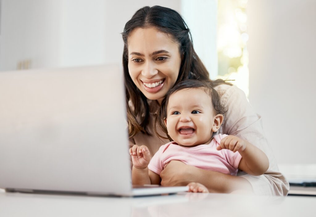 A happy mother holding her baby smiling at her laptop on a video call