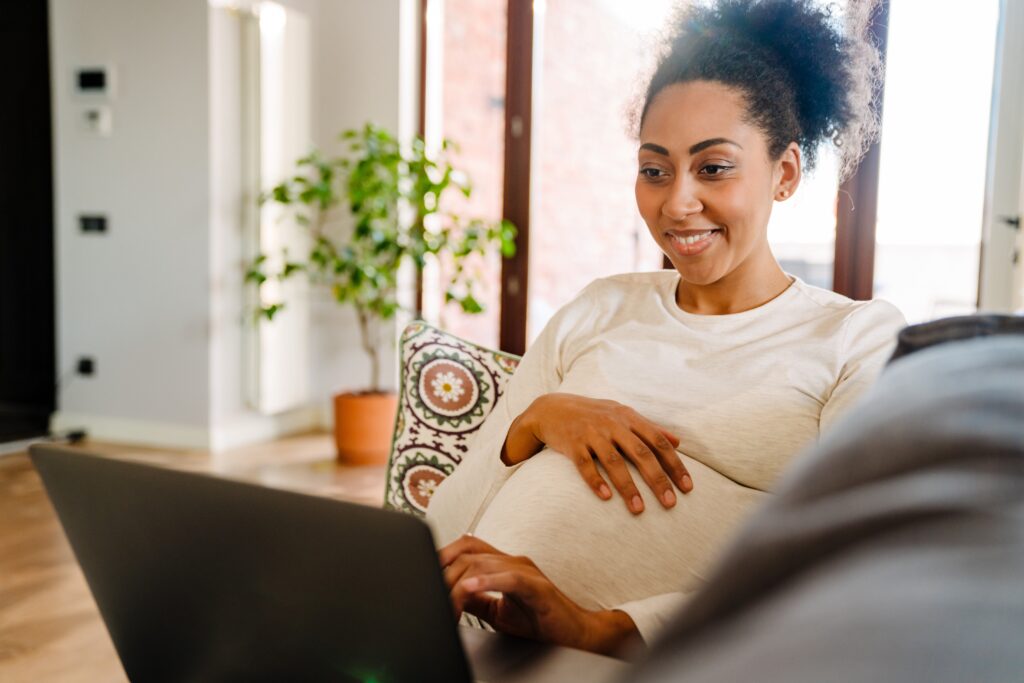 Pregnant woman smiling while using her laptop with her hand on her bump